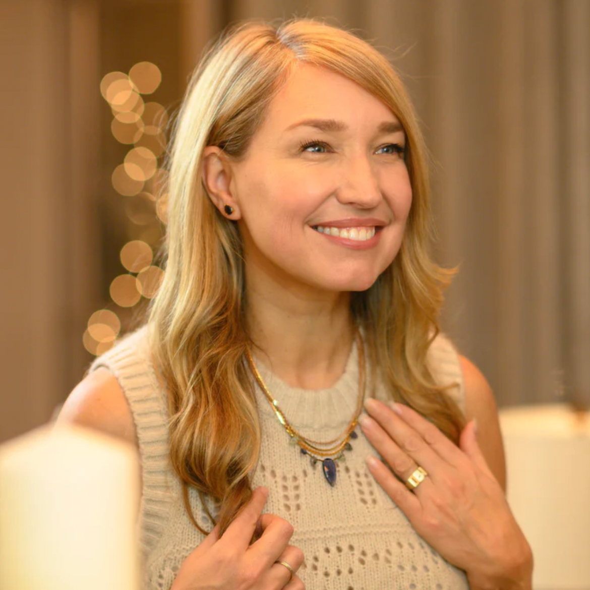 Dayna Manning is shown wearing sparkly pants and a camisole with the same silver sequin. She plays a guitar.