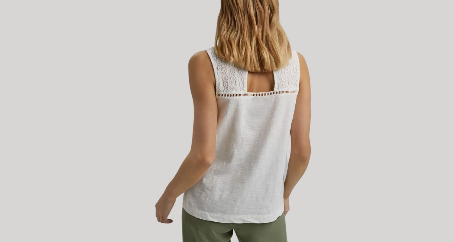 A woman is shown wearing a white sleeveless top. She faces away from the camera so we can see a cutout in the top of the back.