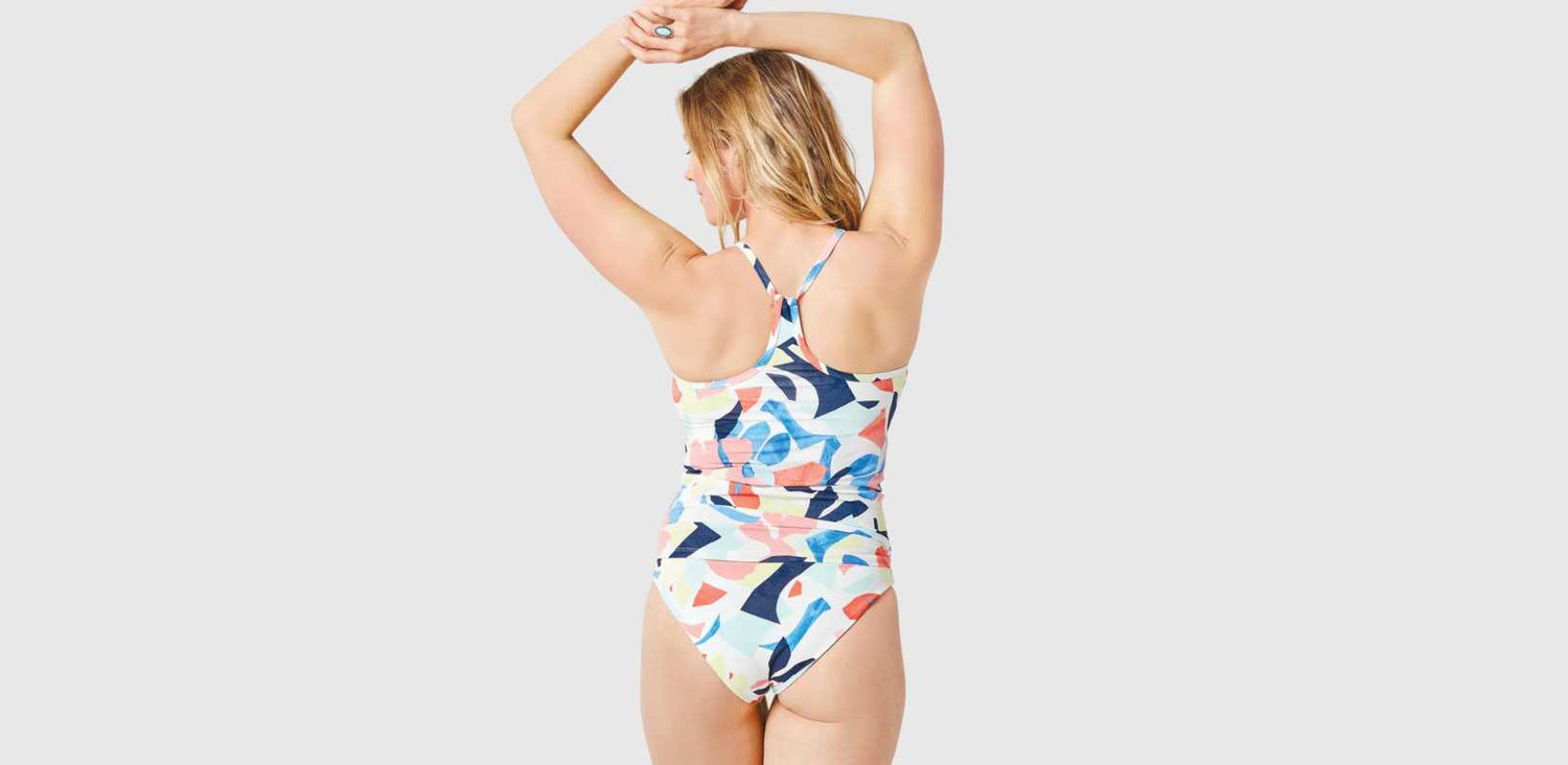 A woman's back is shown. She wears a one piece swimsuit with a multicoloured pattern.
