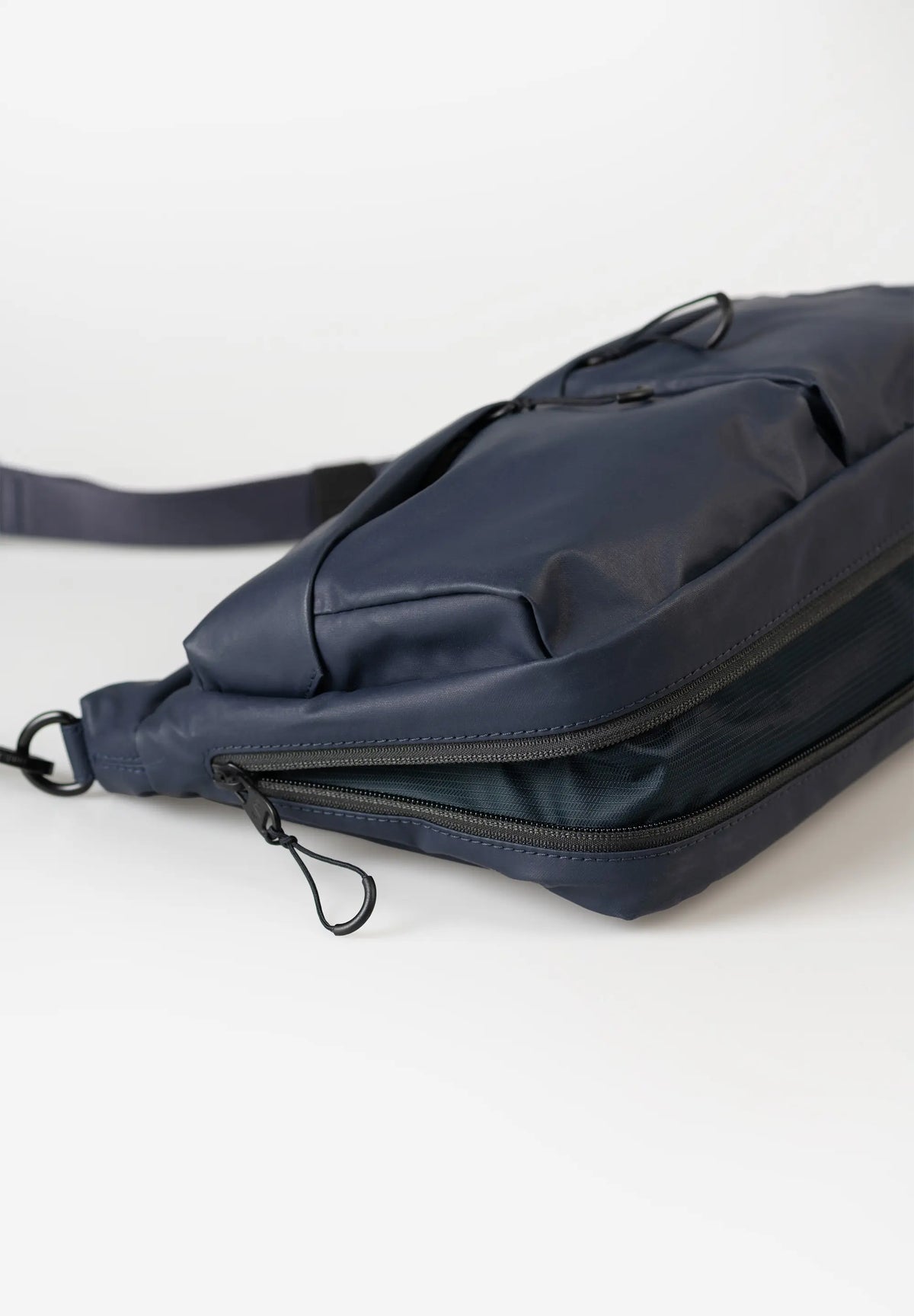 Aunts & Uncles Mogami RE Lite Crossbody Bag. A navy blue nylon crossbody bag with a zippered pocket and adjustable strap, photographed on a clean white background.