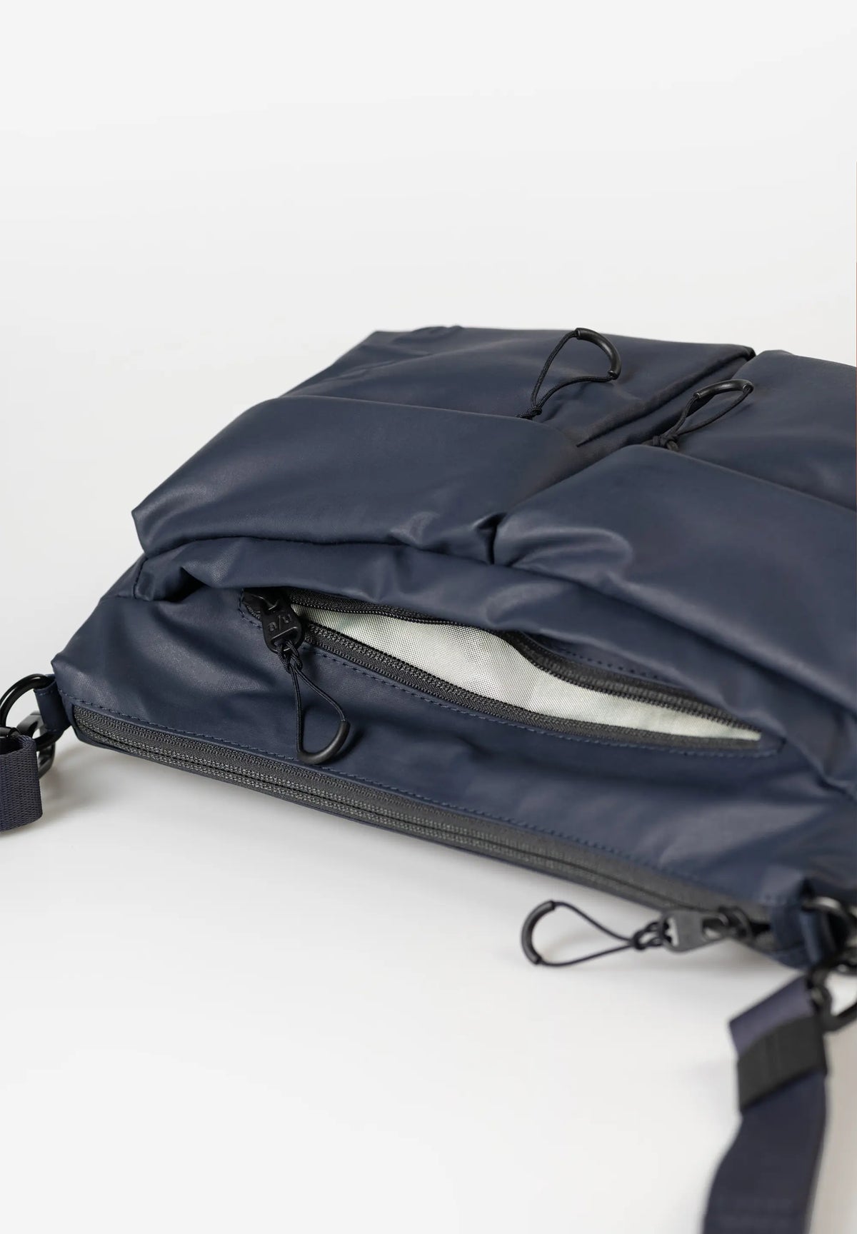 Aunts & Uncles Mogami RE Lite Crossbody Bag. A close-up of a navy blue nylon messenger bag with multiple zippered compartments and black hardware, shown on a clean white background.