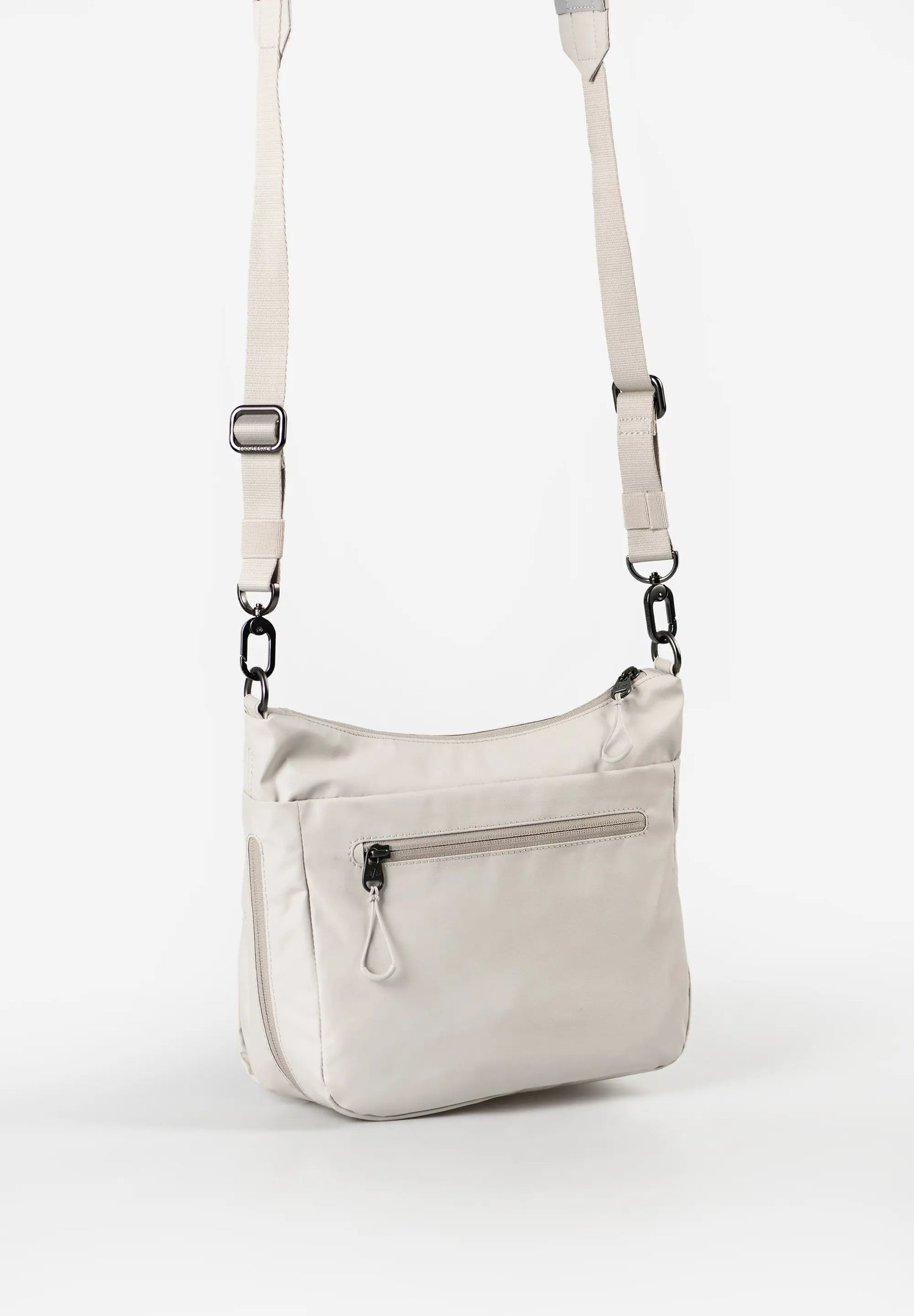 Aunts & Uncles Nanuki RE Lite Crossbody Bag. A light beige nylon crossbody bag with a matching adjustable shoulder strap, featuring a front zippered pocket and black metal hardware, shown against a plain white background.