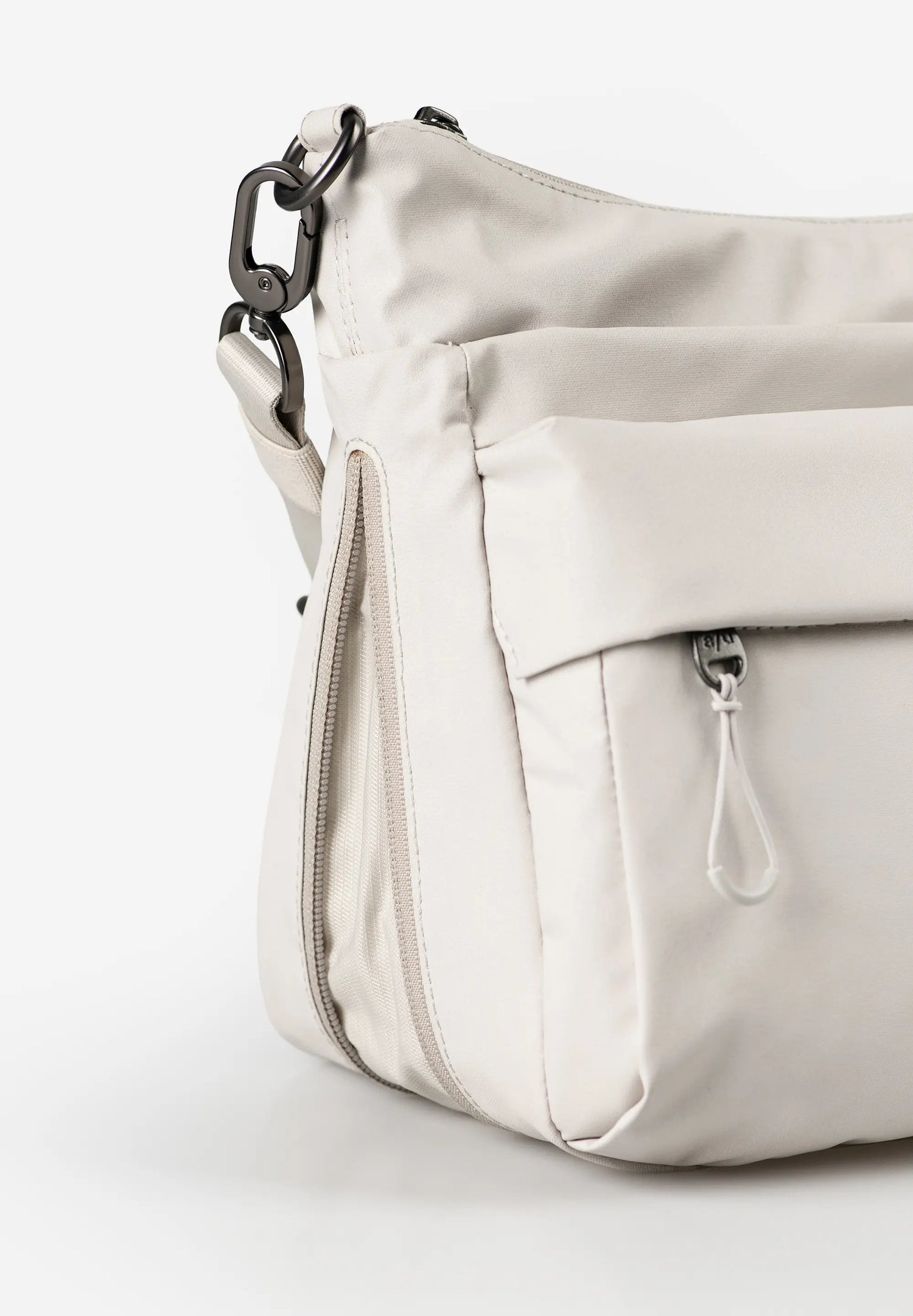 Aunts & Uncles Nanuki RE Lite Crossbody Bag. A close-up of a light beige nylon shoulder bag with a front zippered pocket and a black metal chain link detail, set against a plain white background.