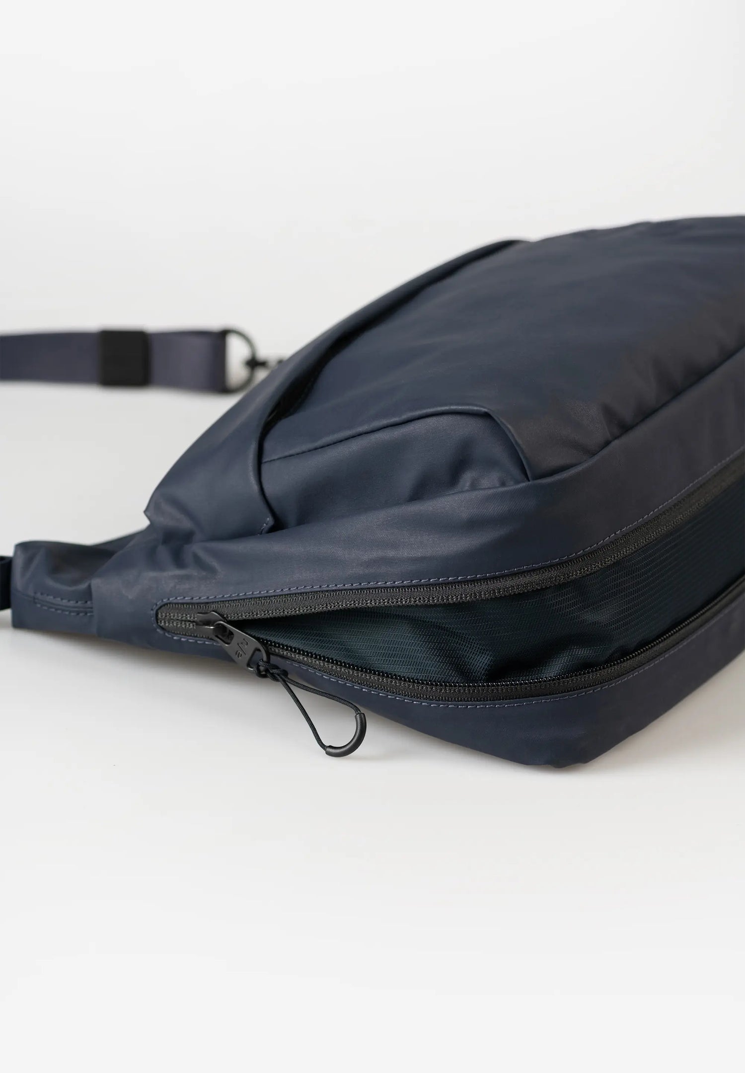 Aunts & Uncles Nanuki RE Lite Crossbody Bag. A dark navy blue nylon crossbody bag with a zippered compartment and adjustable strap, shown on a clean white background.