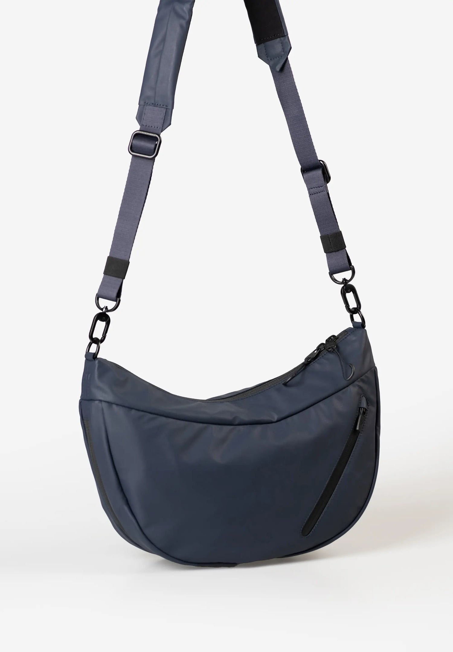 Aunts & Uncles Toyo RE Lite Halfmoon Bag. A navy blue crescent-shaped shoulder bag with a matching adjustable shoulder strap and black hardware, shown against a plain white background.