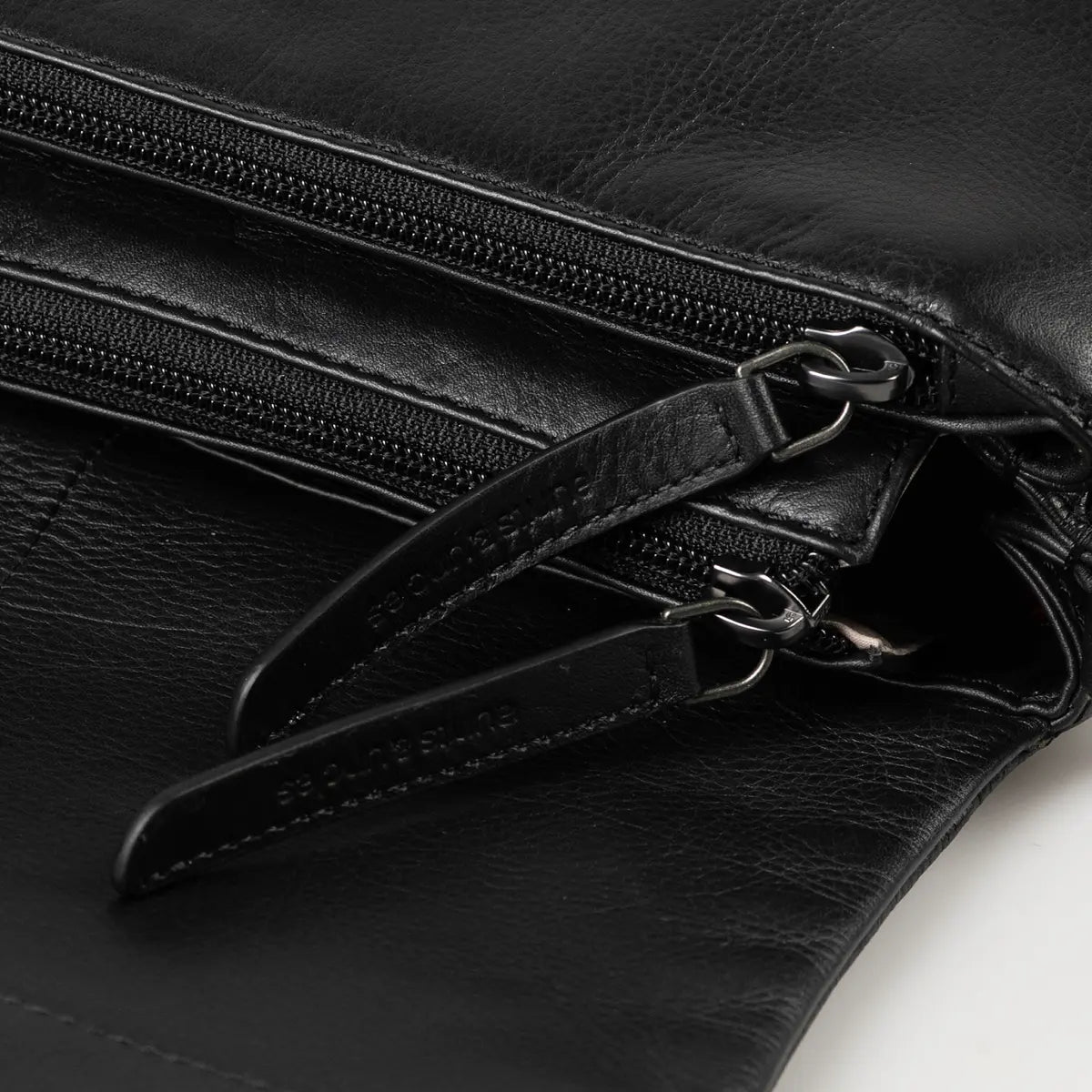 Aunts & Uncles Fern Leather Crossbody Purse. Close-up of a black leather bag with dual zipper compartments and silver-tone hardware, showing a small embossed brand mark on the zipper pull.