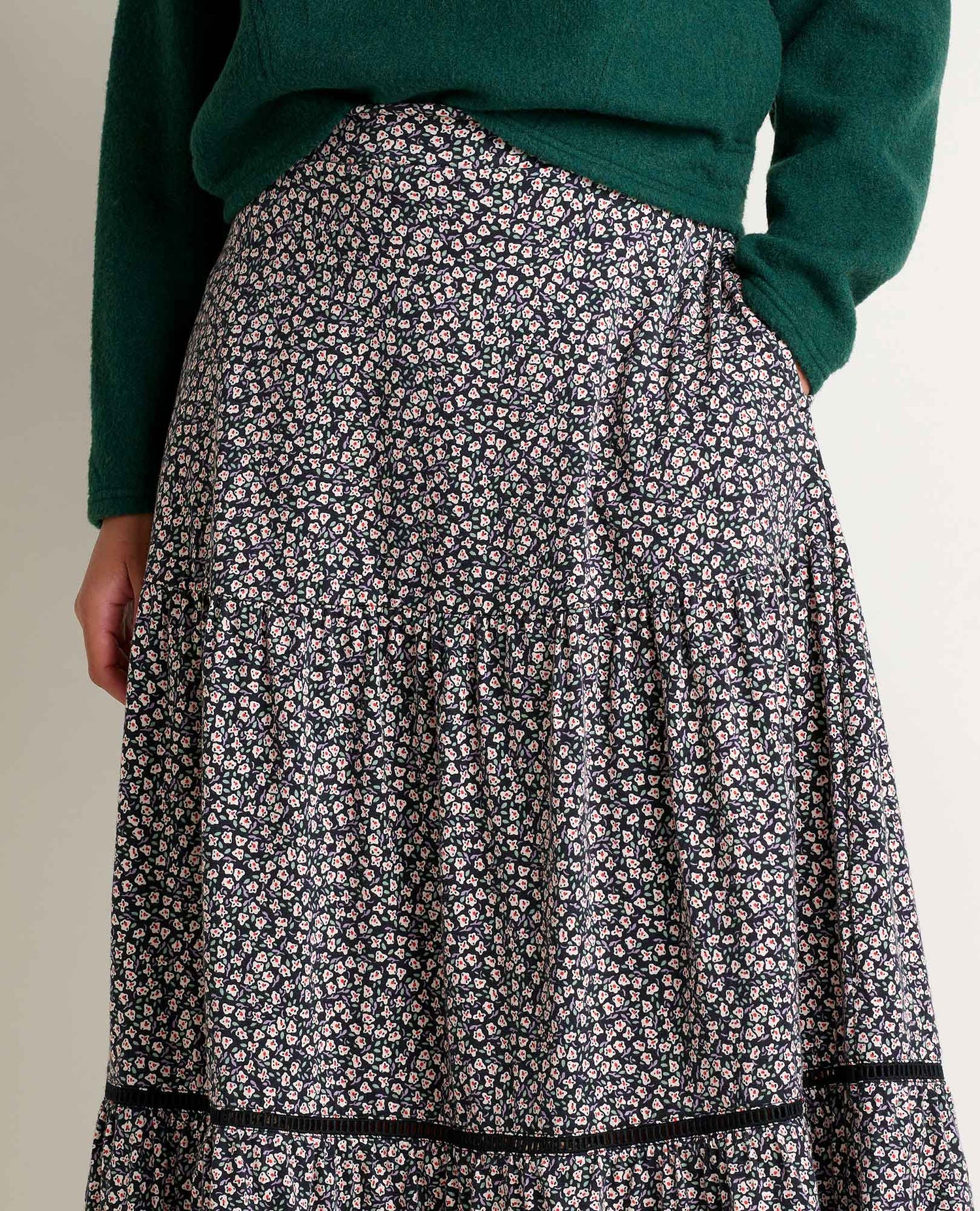 Person wearing a green sweater and floral skirt on a neutral background