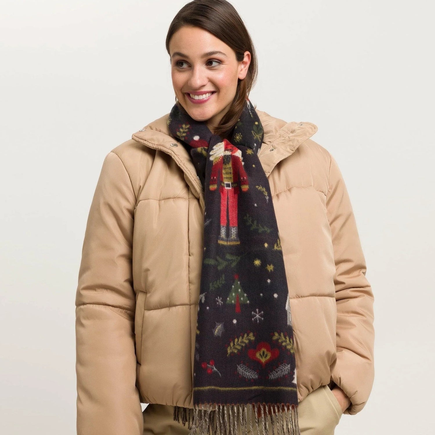 A woman wears a scarf with a Christmas elf and holiday symbols. 