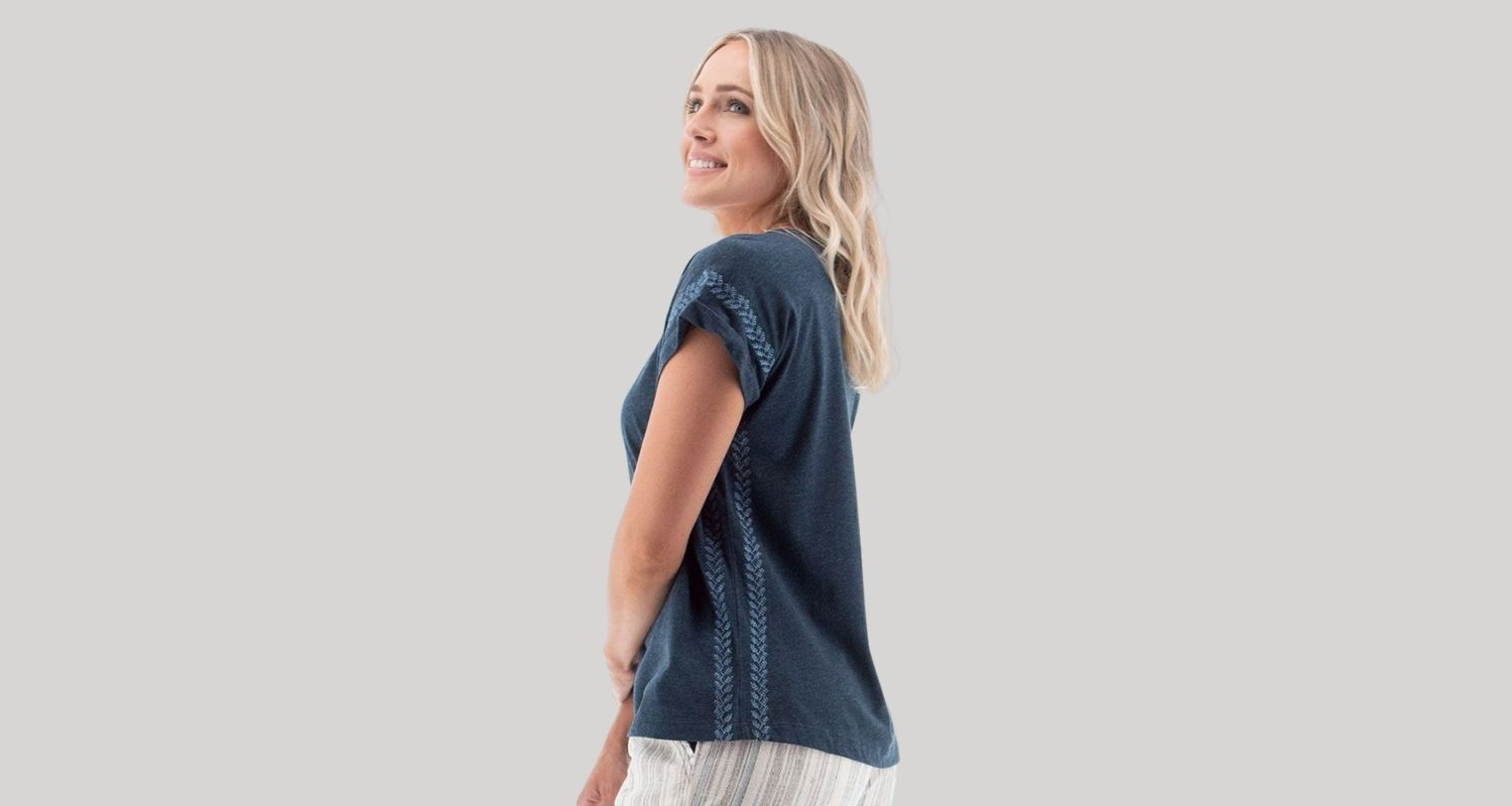 A woman wears a navy blue T-shirt with short sleeves and stich detail at the sleeve and down the side of the torso.