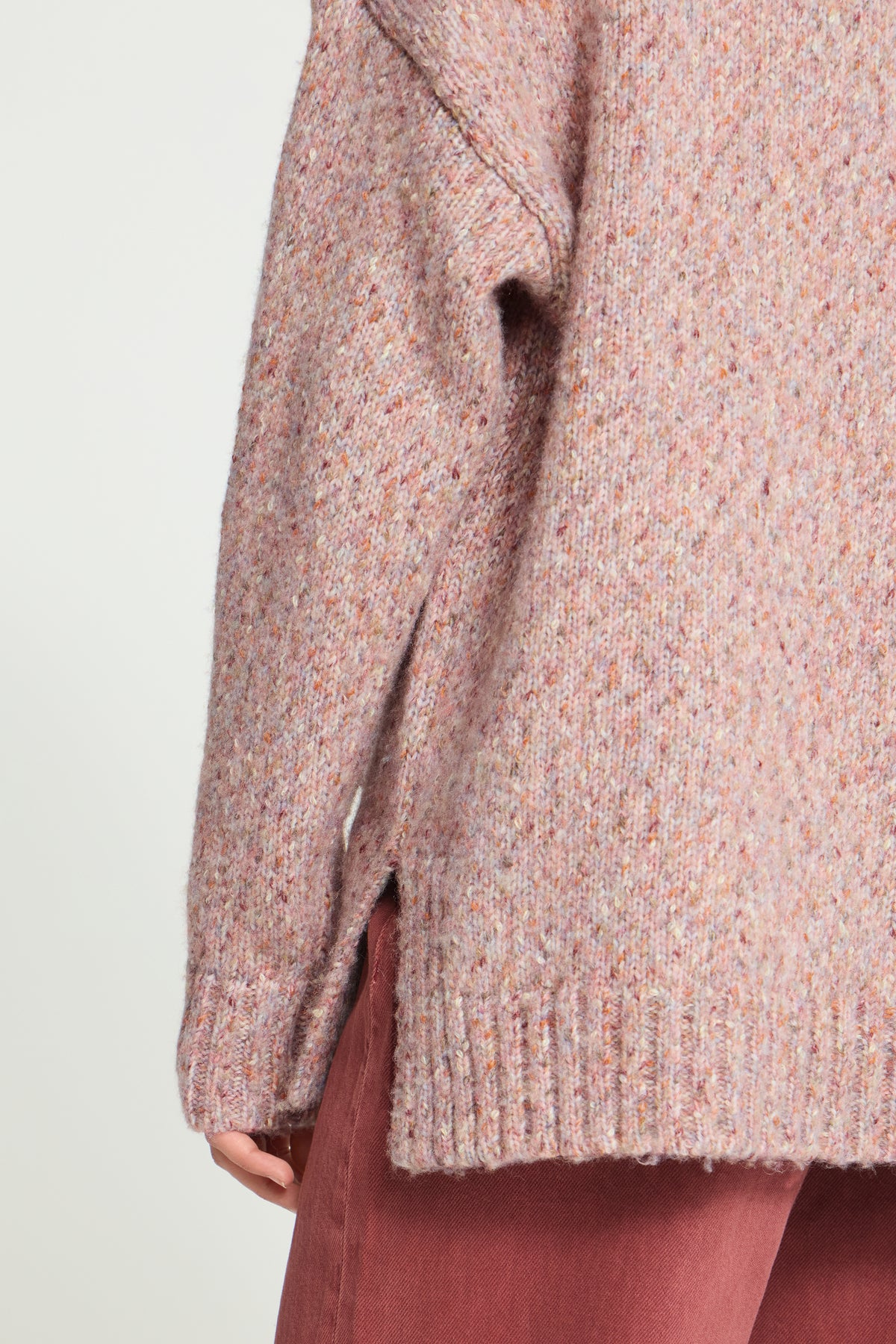 Ichi Fanny Sweater. Close-up of a person wearing a chunky knit sweater in a heathered dusty pink and peach tone, paired with mauve-brown pants, against a plain light background.