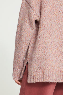Ichi Fanny Sweater. Close-up of a person wearing a chunky knit sweater in a heathered dusty pink and peach tone, paired with mauve-brown pants, against a plain light background.