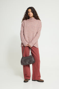 Ichi Fanny Sweater. A woman modeling a chunky knit turtleneck sweater in dusty rose pink, paired with rust-colored wide-leg trousers and a dark gray textured shoulder bag, against a plain white studio background.