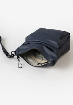 Aunts & Uncles Yura RE Lite Crossbody Bag. A navy blue nylon crossbody bag with an open zipper revealing a light gray interior, shown on a clean white background.