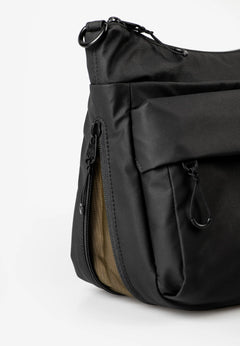 Aunts & Uncles Nanuki RE Lite Crossbody Bag. A close-up of a black nylon shoulder bag with multiple zippered pockets and a side zipper revealing a tan interior lining, set against a plain white background.