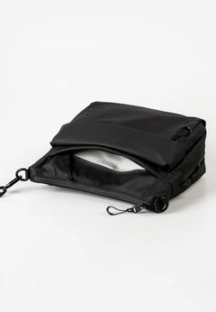 Aunts & Uncles Nanuki RE Lite Crossbody Bag. A black nylon pouch or small bag with a zippered closure and a flap, shown open on a clean white studio background.
