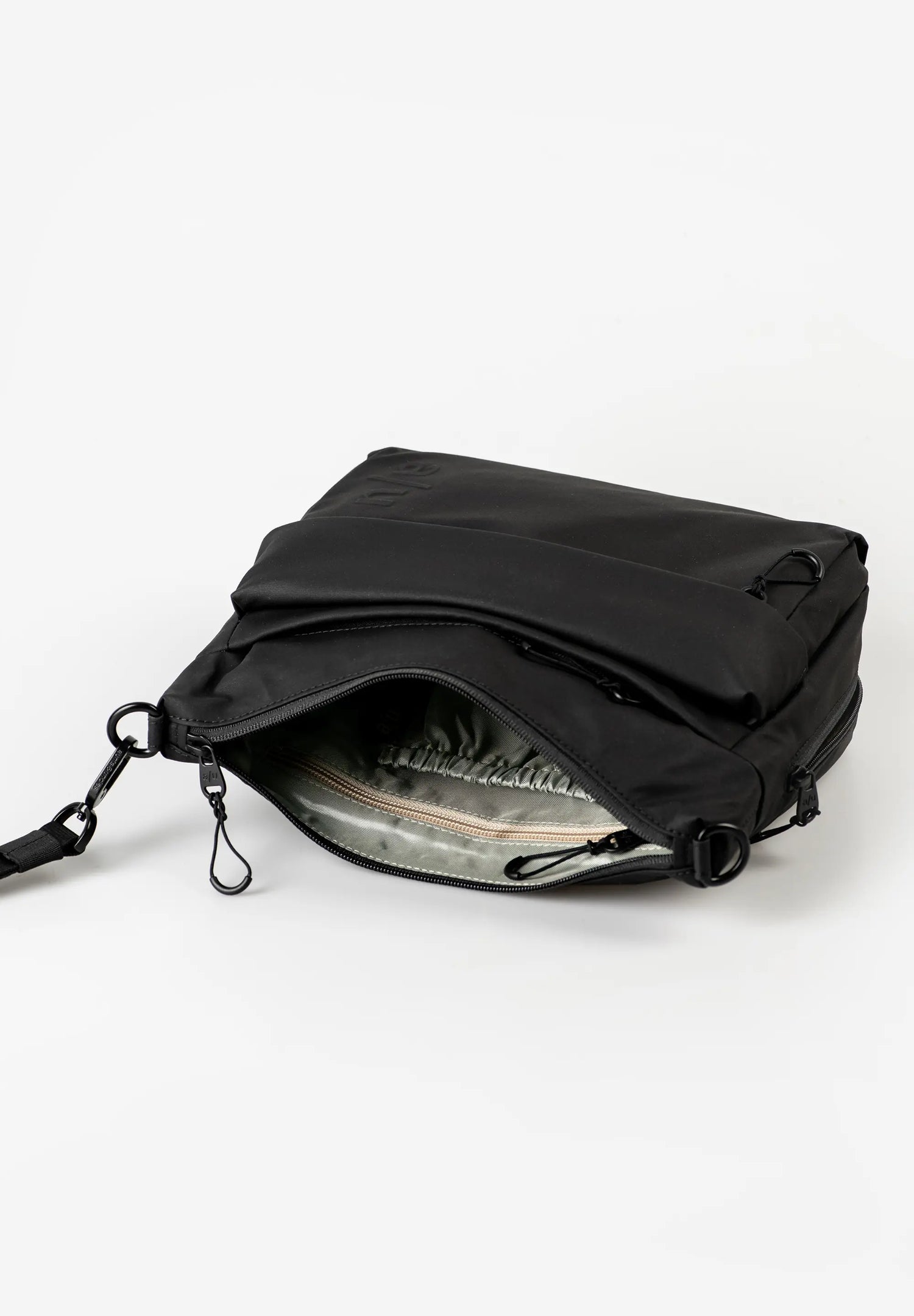 Aunts & Uncles Nanuki RE Lite Crossbody Bag. A black nylon messenger bag shown open, displaying its interior lining and zipper compartments, set against a plain white studio background.