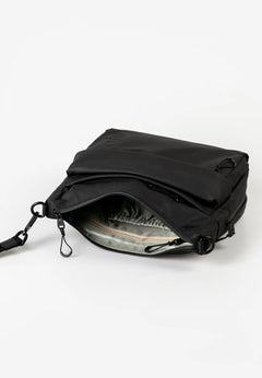 Aunts & Uncles Nanuki RE Lite Crossbody Bag. A black nylon messenger bag shown open, displaying its interior lining and zipper compartments, set against a plain white studio background.