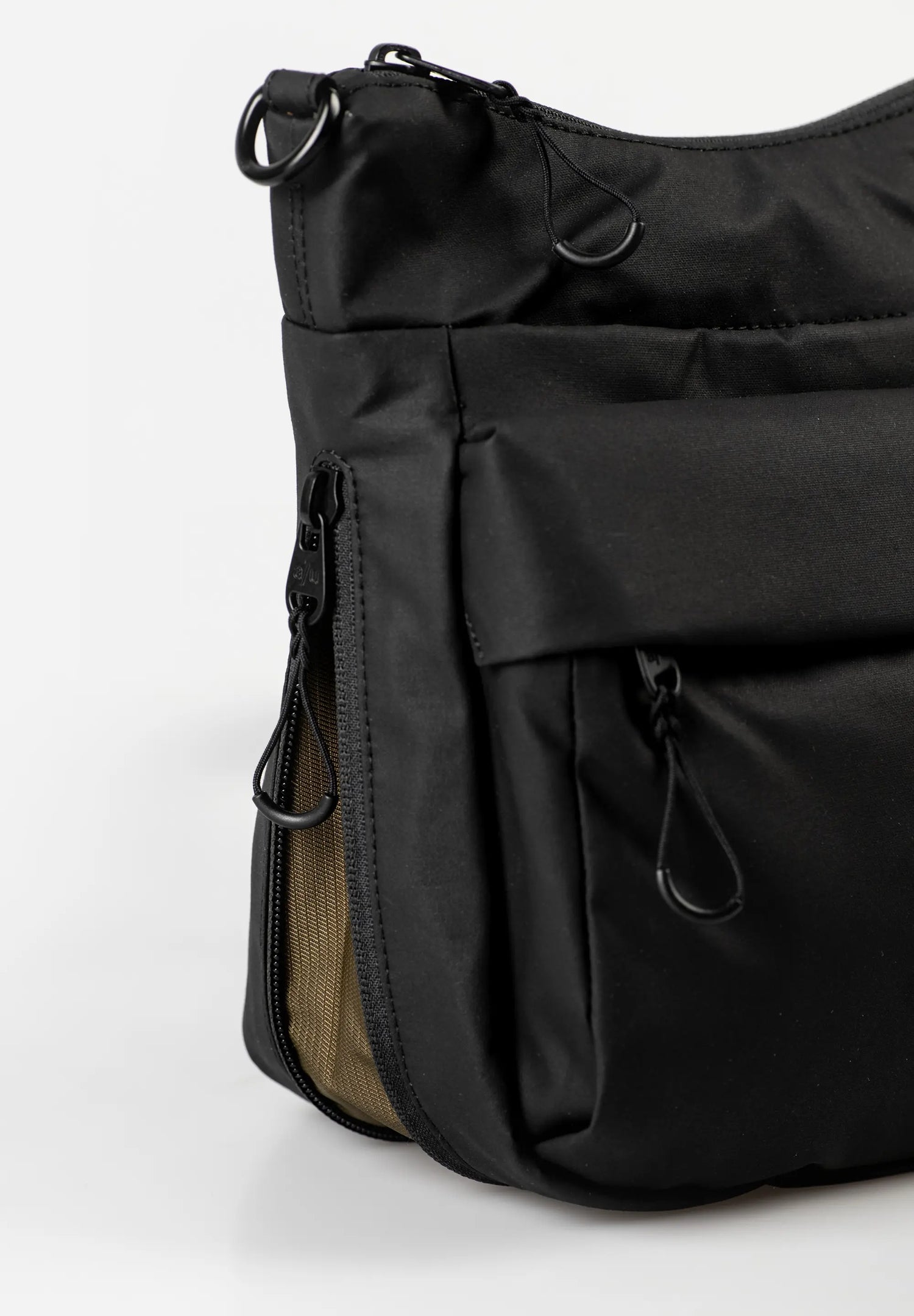 Aunts & Uncles Yura RE Lite Crossbody Bag.Close-up of a black nylon shoulder bag with multiple zippered pockets and black metal hardware, set against a plain white background.