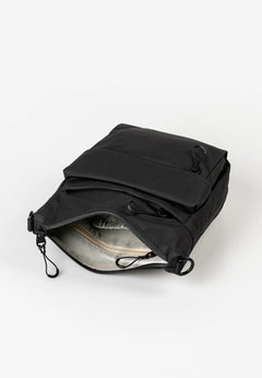 Aunts & Uncles Yura RE Lite Crossbody Bag.A black nylon crossbody bag shown open, displaying its interior lining and zippered compartments, set against a plain white background.