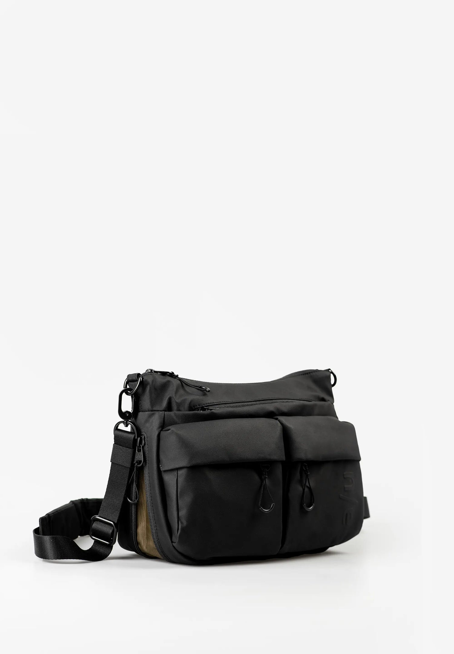 Aunts & Uncles Mogami RE Lite Crossbody Bag. A black nylon messenger bag with multiple front pockets and an adjustable shoulder strap, photographed on a clean white studio background.