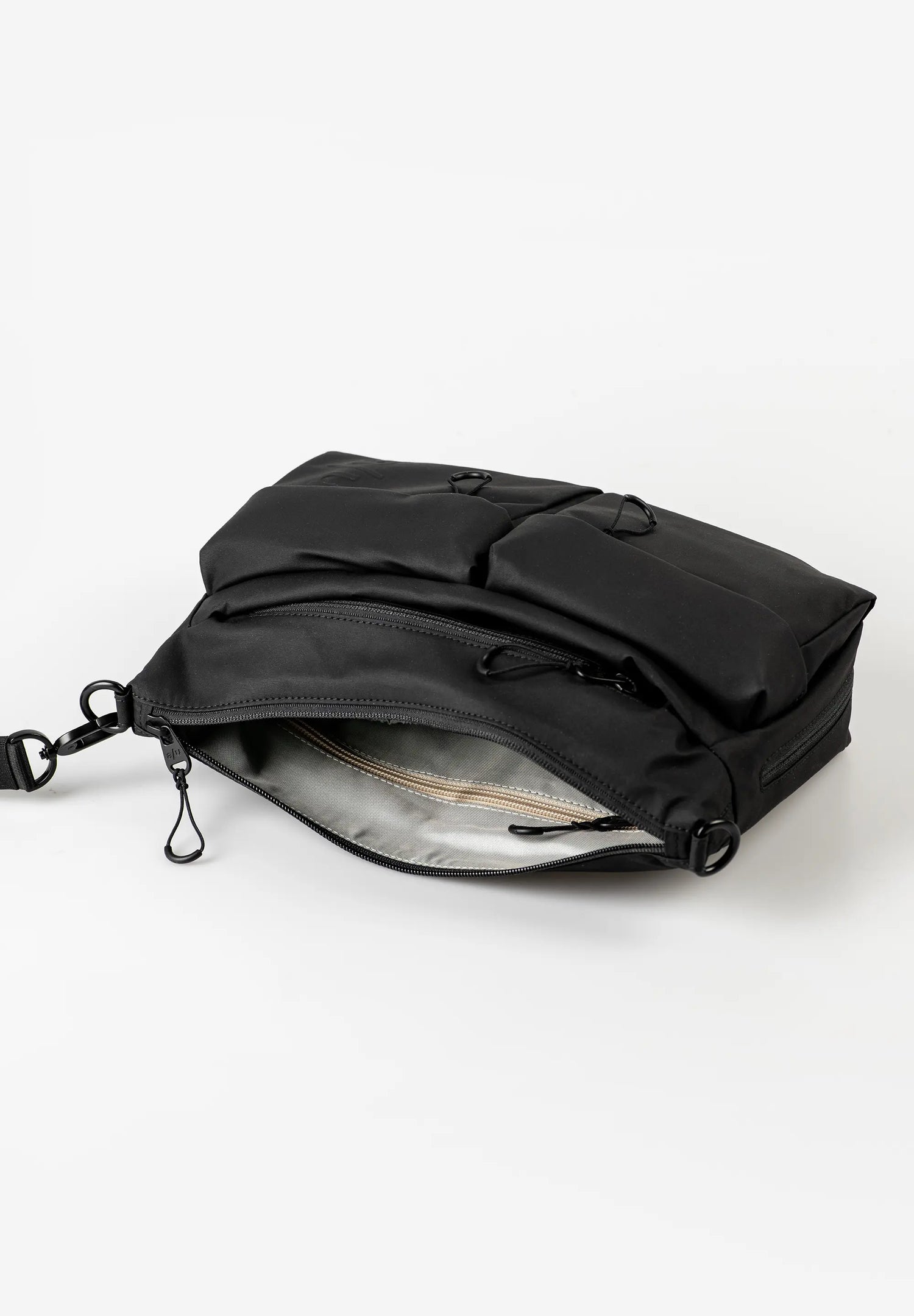 Aunts & Uncles Mogami RE Lite Crossbody Bag. A black nylon utility pouch or small backpack shown open on a clean white background, revealing a light gray interior lining and black zipper pulls.