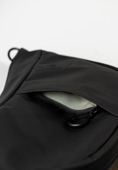 Aunts & Uncles Toyo RE Lite Halfmoon Bag. Close-up of a black fabric bag with a partially unzipped pocket showing a light gray interior lining.