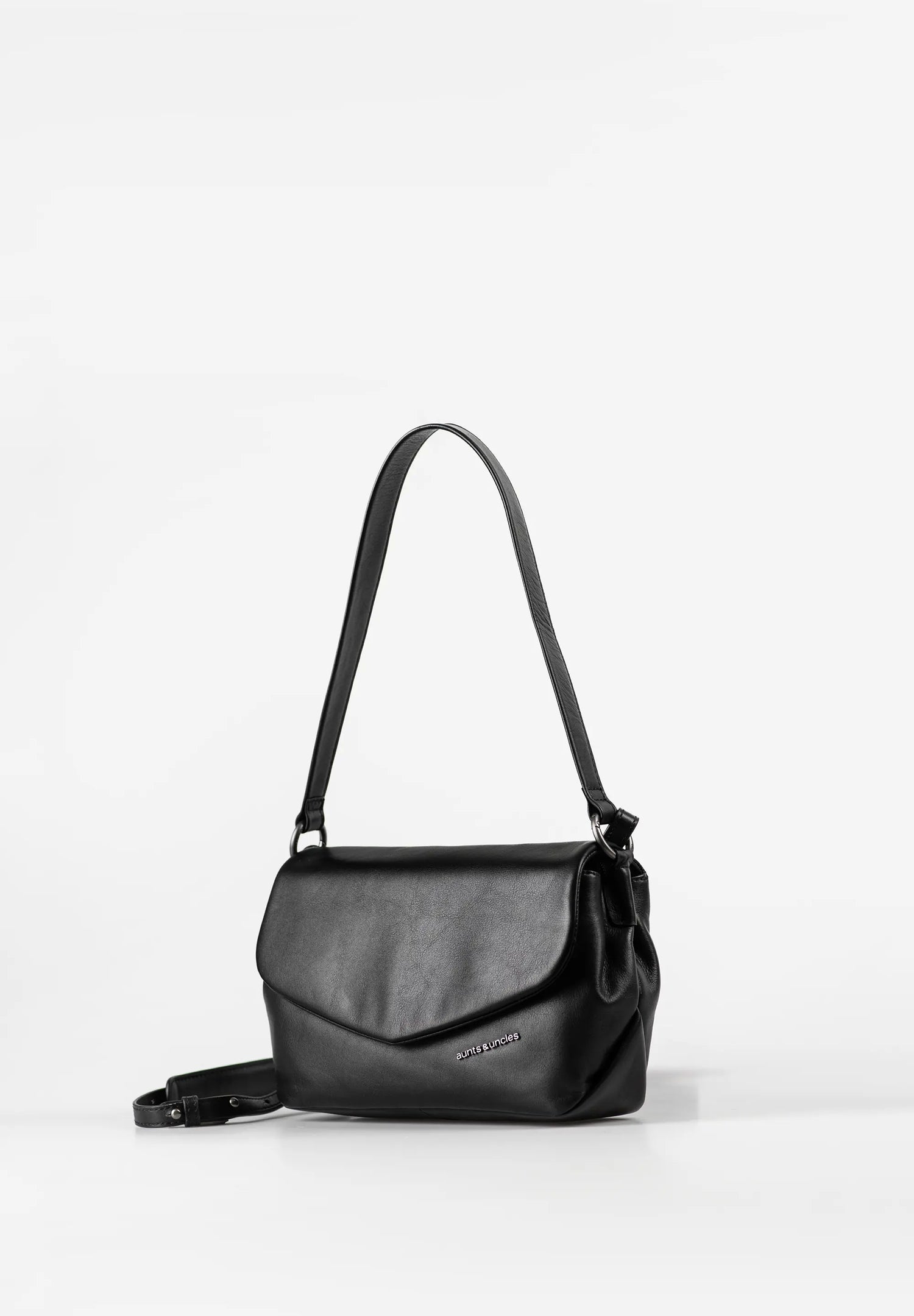 Aunts & Uncles Fern Leather Crossbody Purse. A black leather shoulder bag with a flap front and a long shoulder strap, photographed on a clean white studio background.