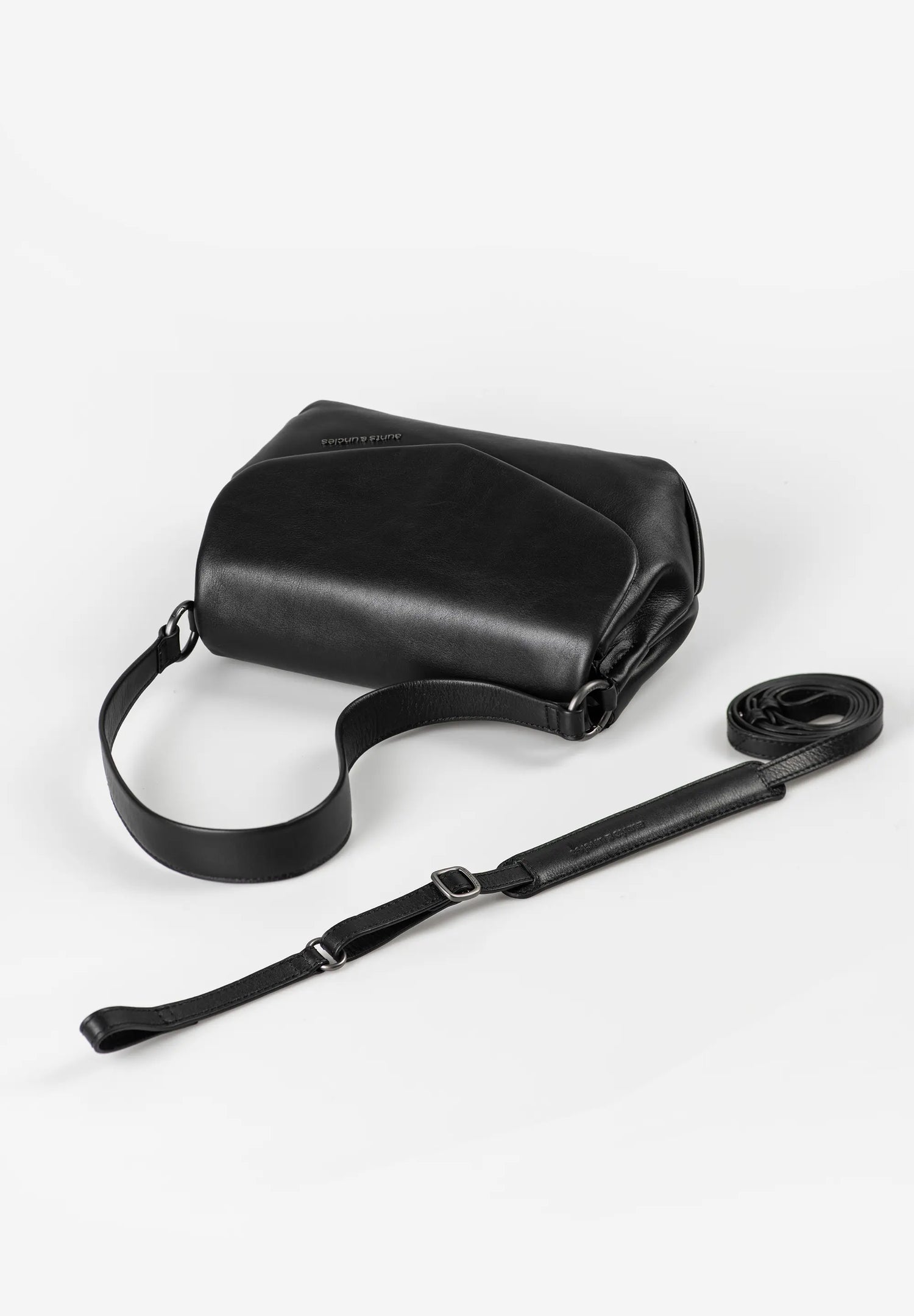 Aunts & Uncles Fern Leather Crossbody Purse. Black leather bag with a strap on a white background