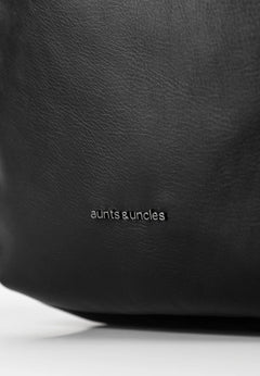 Aunts & Uncles Coco Leather Backpack Purse. Close-up of a black textured leather bag with the 'aunts & uncles' logo printed in white near the bottom center.