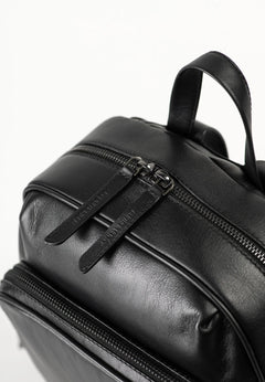 Aunts & Uncles Coco Leather Backpack Purse.  Close-up of a black leather backpack showing a front zippered pocket with a pull tab and a top carry handle against a white background.