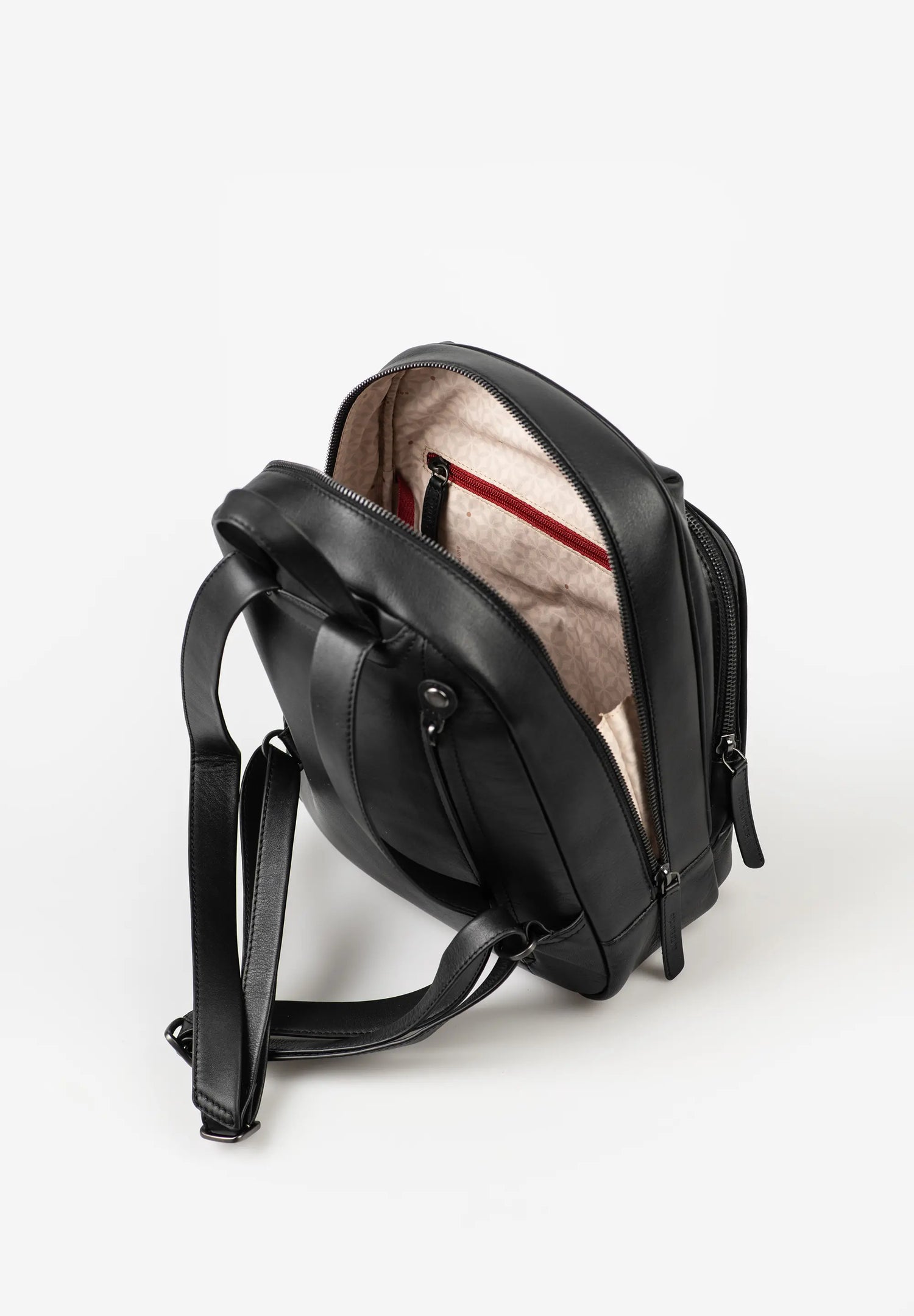 Aunts & Uncles Coco Leather Backpack Purse.  A black leather backpack shown open from a side angle, revealing a beige interior lining with a red accent stripe inside, set against a plain white background.