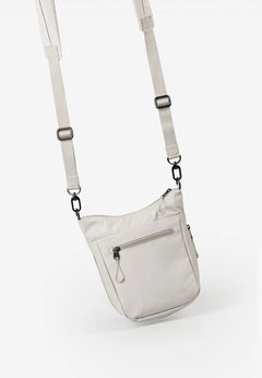 Aunts & Uncles Yura RE Lite Crossbody Bag.A light beige nylon shoulder bag with a matching adjustable shoulder strap and black metal hardware, shown against a plain white background.