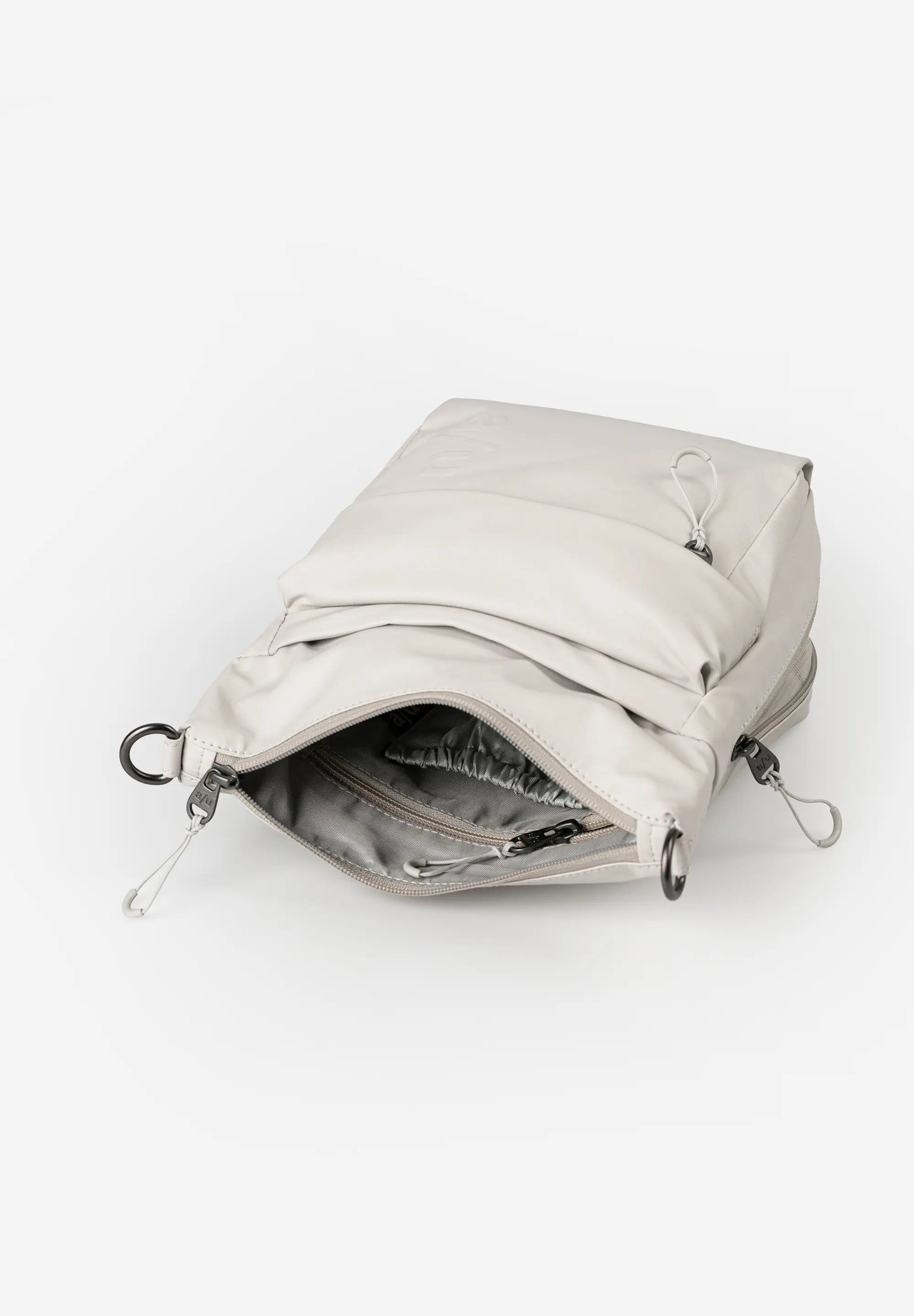 Aunts & Uncles Yura RE Lite Crossbody Bag. A light beige puffer-style pouch bag shown open, revealing a gray interior lining and silver metal zipper hardware, on a clean white background.