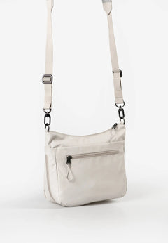 Aunts & Uncles Nanuki RE Lite Crossbody Bag. A light beige nylon crossbody bag with a matching adjustable shoulder strap, featuring a front zippered pocket and black metal hardware, shown against a plain white background.