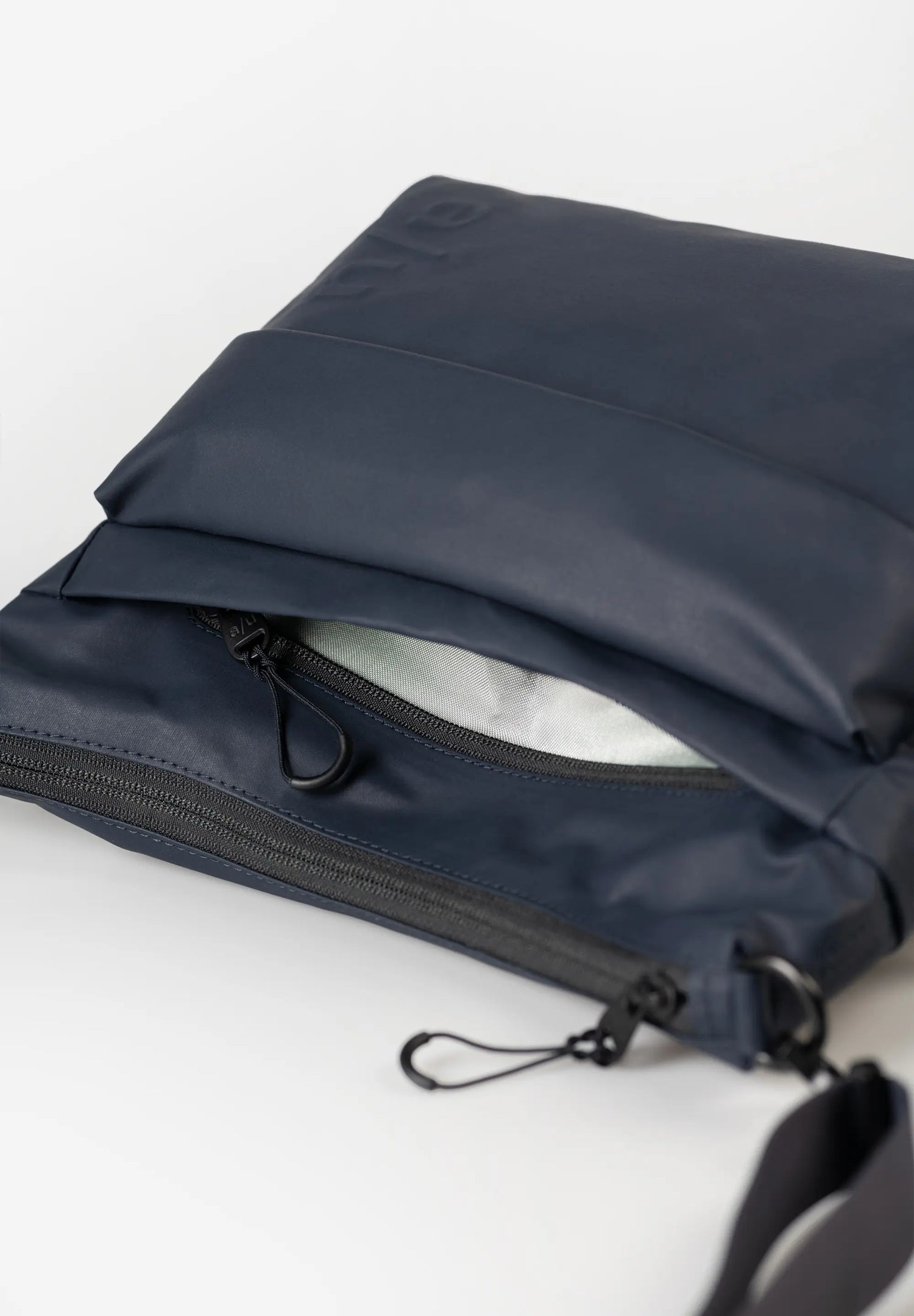Aunts & Uncles Nanuki RE Lite Crossbody Bag. A navy blue waterproof pouch or small bag with a black zipper and black strap, shown open on a clean white background.