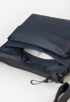 Aunts & Uncles Nanuki RE Lite Crossbody Bag. A navy blue waterproof pouch or small bag with a black zipper and black strap, shown open on a clean white background.