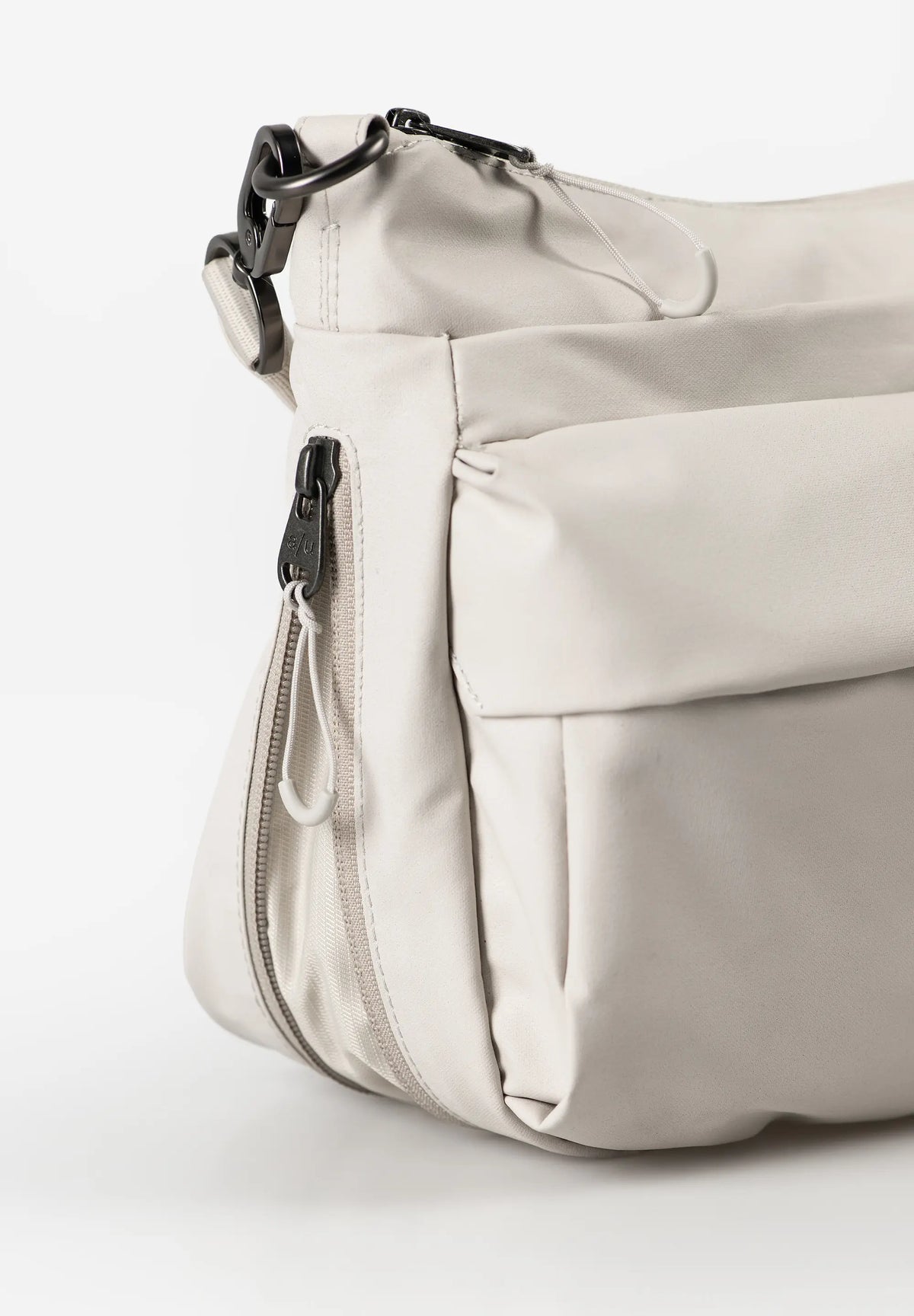 Aunts & Uncles Mogami RE Lite Crossbody Bag. A close-up of a light beige nylon shoulder bag with black hardware, showing a front zippered pocket and a side zipper pull.