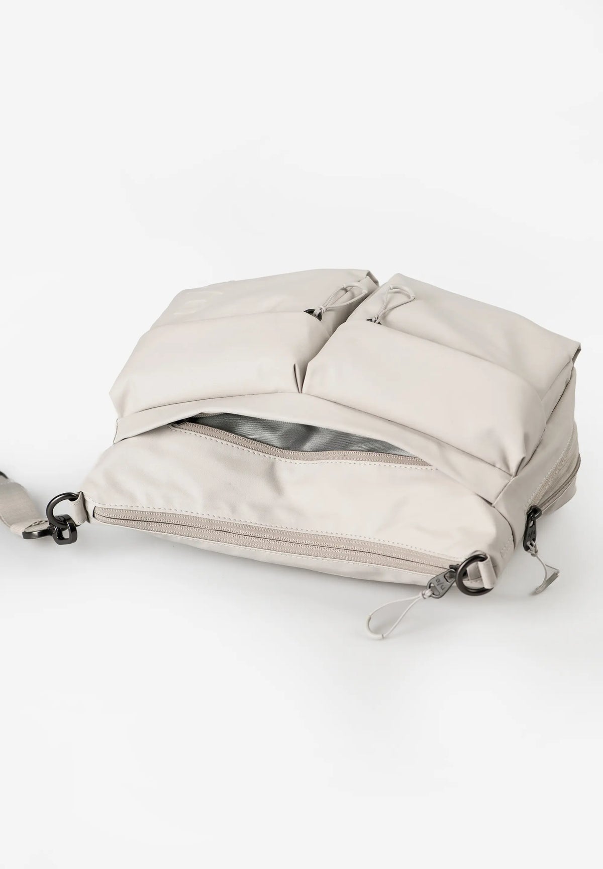 Aunts & Uncles Mogami RE Lite Crossbody Bag. A light beige nylon backpack with multiple zippered compartments and a gray interior lining, shown on a clean white background.