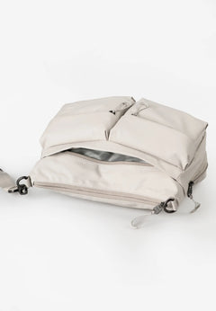 Aunts & Uncles Mogami RE Lite Crossbody Bag. A light beige nylon backpack with multiple zippered compartments and a gray interior lining, shown on a clean white background.
