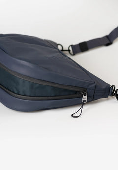 Aunts & Uncles Toyo RE Lite Halfmoon Bag. A navy blue nylon crossbody bag with a zippered compartment and adjustable strap, shown on a clean white background.