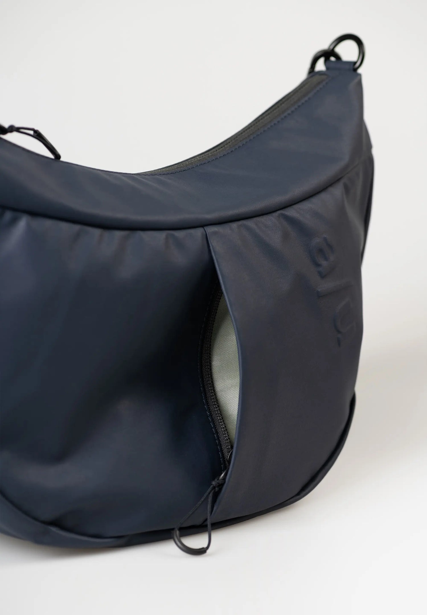 Aunts & Uncles Toyo RE Lite Halfmoon Bag. A dark navy blue crescent-shaped shoulder bag with a zippered front pocket, shown on a clean white background.