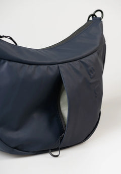 Aunts & Uncles Toyo RE Lite Halfmoon Bag. A dark navy blue crescent-shaped shoulder bag with a zippered front pocket, shown on a clean white background.