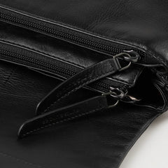 Aunts & Uncles Fern Leather Crossbody Purse. Close-up of a black leather bag with dual zipper compartments and silver-tone hardware, showing a small embossed brand mark on the zipper pull.