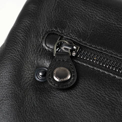Aunts & Uncles Fern Leather Crossbody Purse. Close-up of a black leather bag featuring a silver-tone metal zipper pull with a snap button closure.