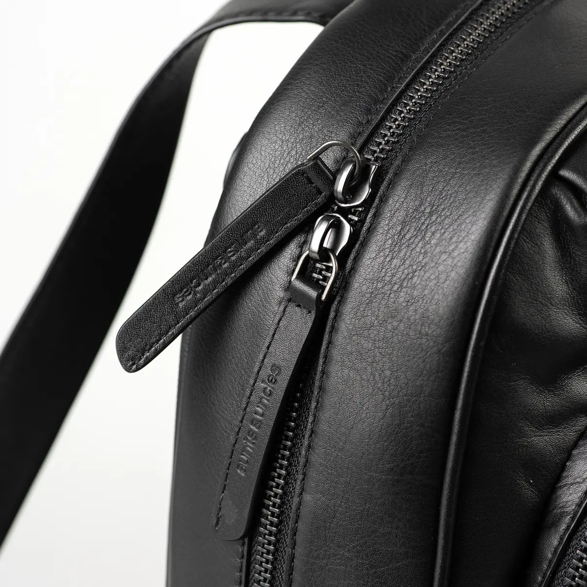 Aunts & Uncles Coco Leather Backpack Purse.  Close-up of a black leather backpack showing a zipper with a branded pull tab that reads 'TWEEL STUDIOS'.