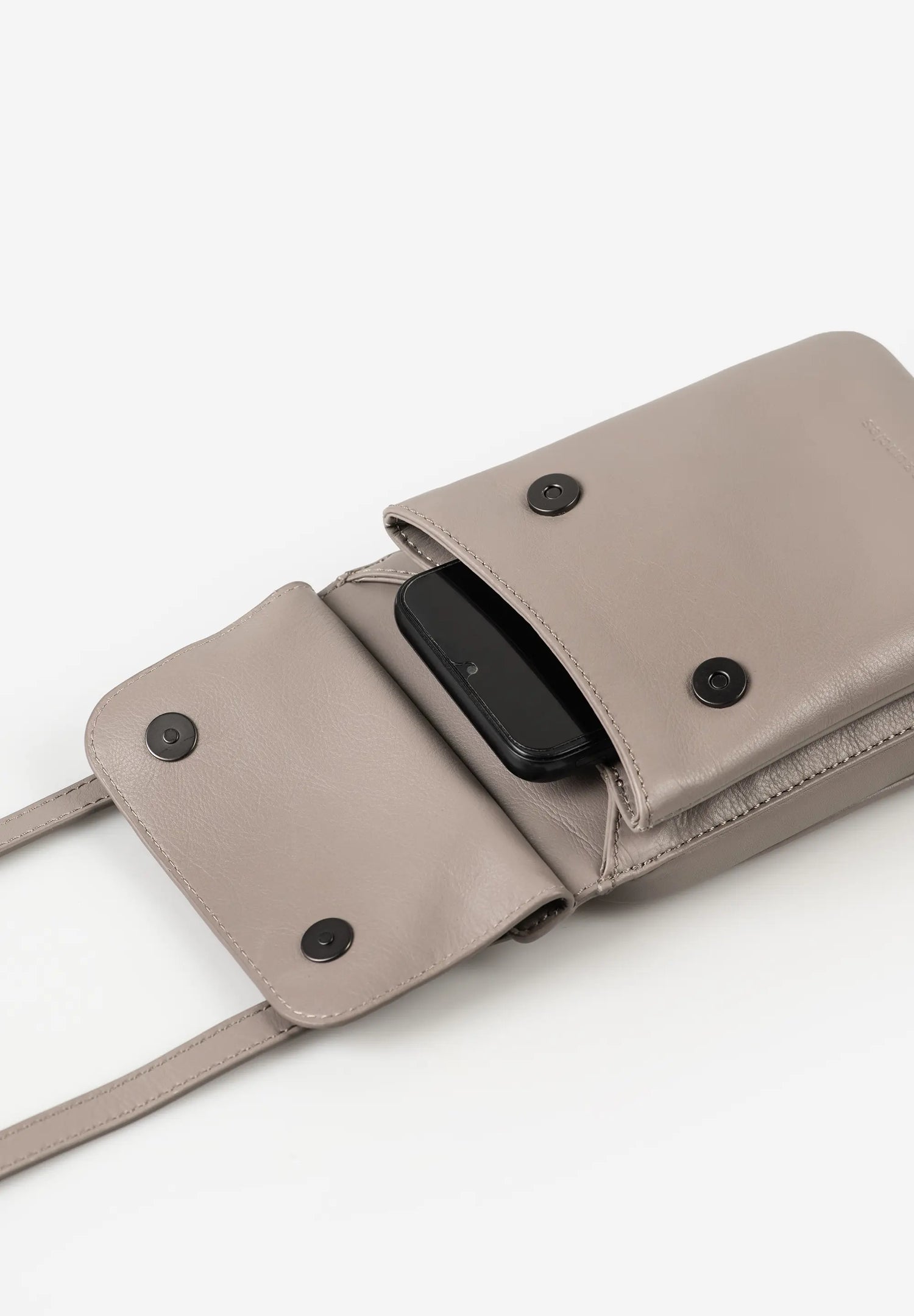 Aunts & Uncles Tulip Leather Phonebag Wallet. A taupe leather crossbody bag with a flap pocket holding a black smartphone, shown on a clean white background.