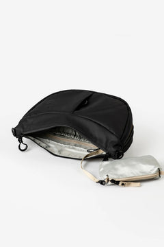 Aunts & Uncles Toyo RE Lite Halfmoon Bag. A black nylon shoulder bag with an open silver-lined interior, shown on a clean white background next to a small metallic silver pouch with a beige strap.